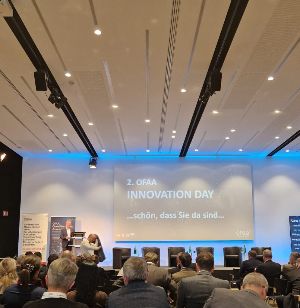 Menschen sitzen in einer Konferenzhalle beim 2. OFAA Innovation Day, Bühne mit Präsentation und Redner.