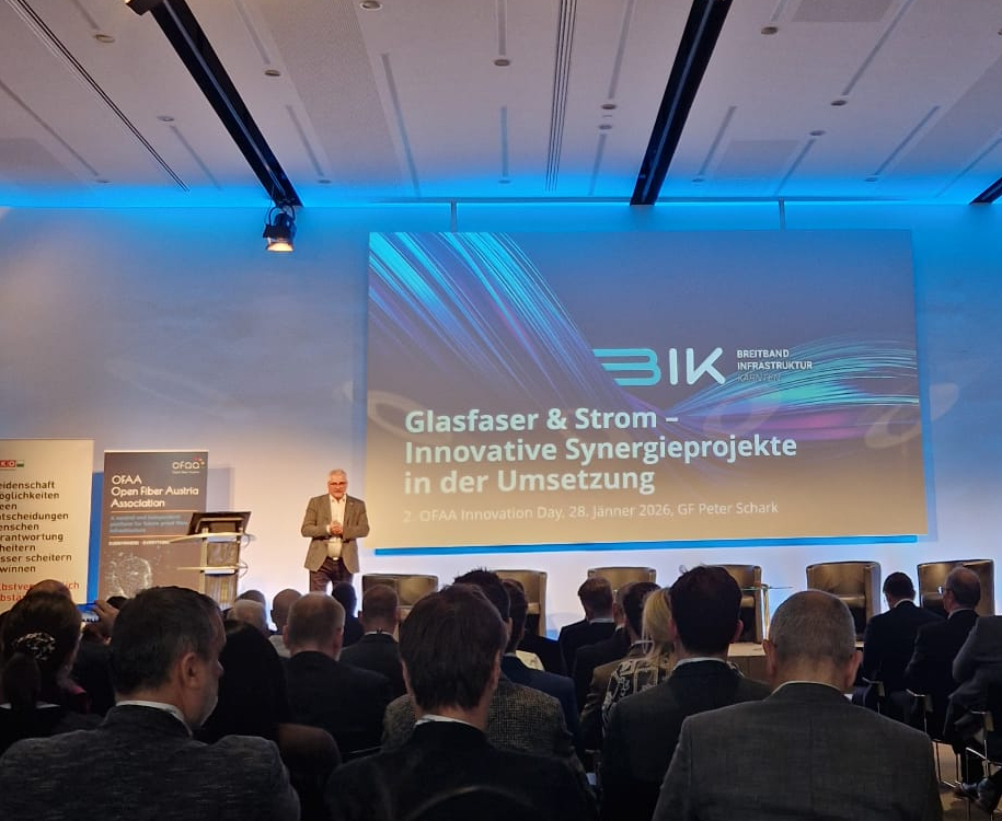 Mann hält Vortrag bei einer Konferenz über Glasfaser und Strom vor Publikum, Präsentation an Leinwand.