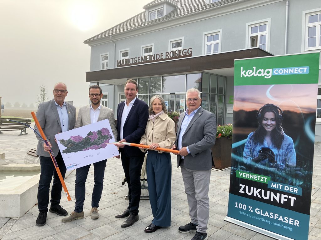 Gruppe von fünf Personen steht mit Karte und Glasfaserrohren vor dem Gebäude der Marktgemeinde Rosegg.